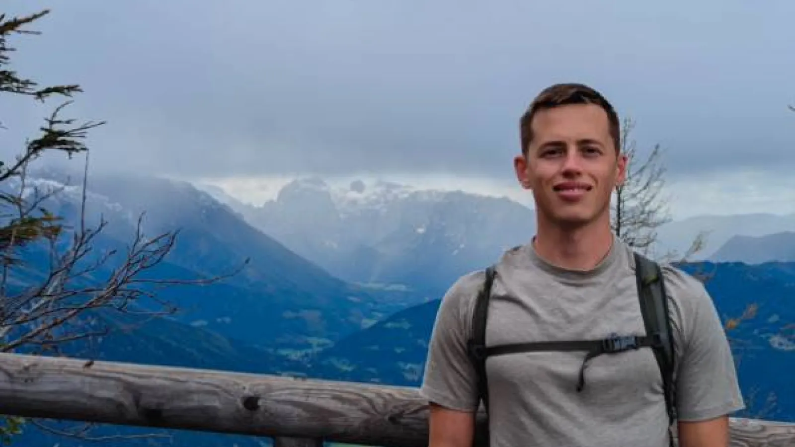 Yasha Shatalov stands wearing a backpack in front of a green mountain landscape