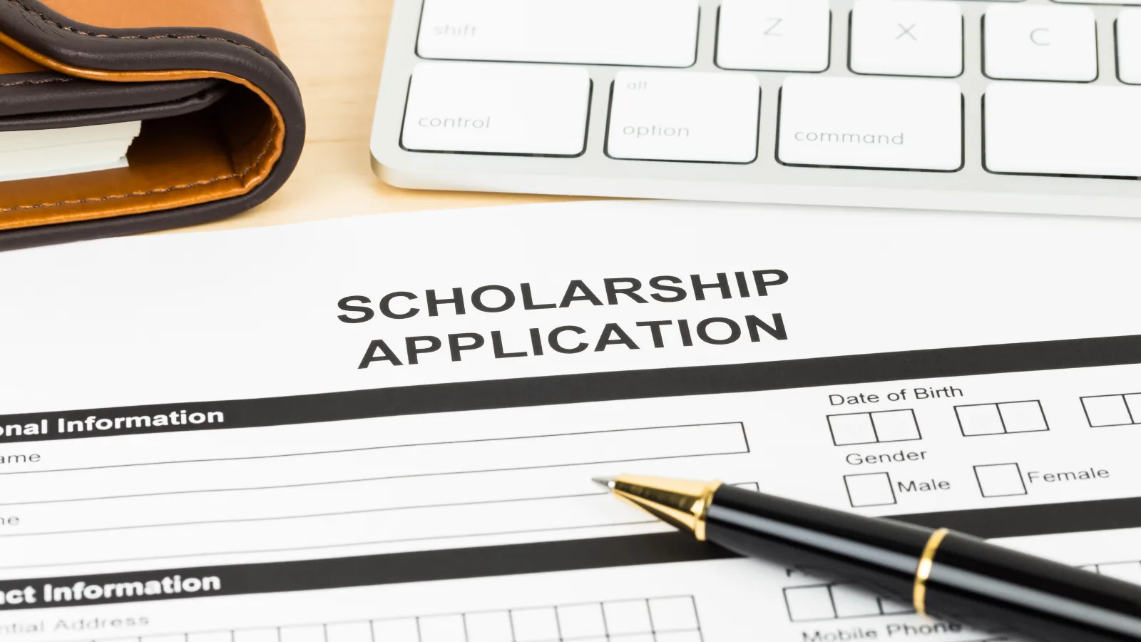 Black scholarship application with a pen on top of it. 