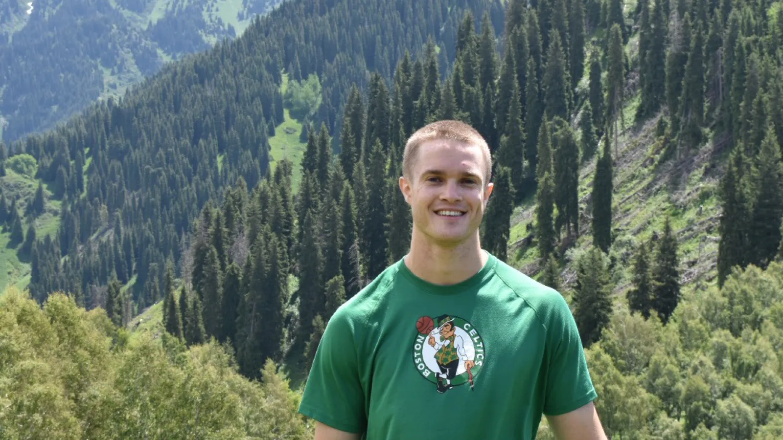 Young man standing and smiling with moutains and forest in the background