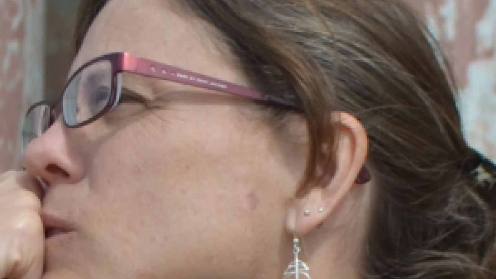 A side profile of a woman's head wearing glasses and dangling earrings