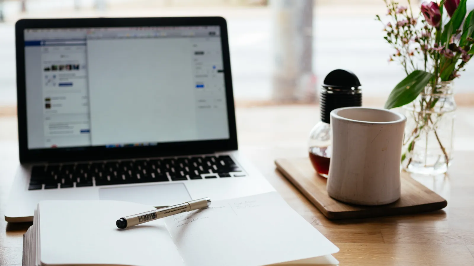Open laptop and notebook with pen laying across it