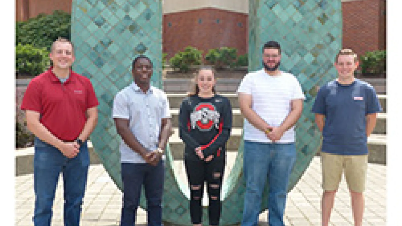 Five people standing shoulder to shoulder with a large tile covered zero behind them